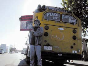 Dave Short holding anti-war poster, and standing in front of old school bus with "peace & justice now!" painted on back windows