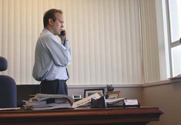 [photo of Paul Gallegos talking on phone behind his desk]