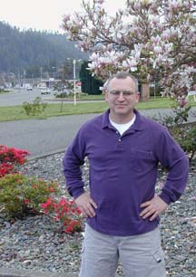 [Jay Parrish standing in front of river-rocked median with blooming tree and shrubs in background]
