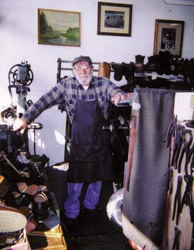Bruno Ravelli in work apron standing in his shoe shop with machines and tools and shoes around him