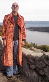 [Doug Wolens in long crushed velvet coat, standing in front of view of river]