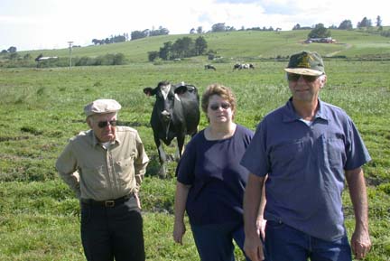 [Petersens standing in field, cow looking on, hills in background]