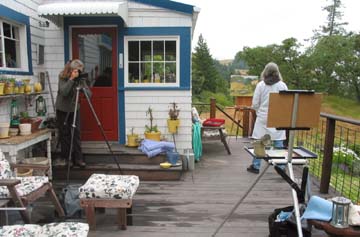 [woman with camera on tripod, woman at easel, on deck of house]