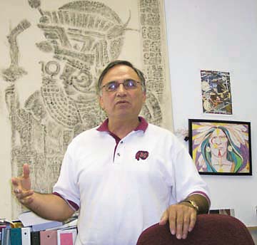 [Arturo Vasquez in his office, Aztec mural and Native American watercolor behind him]
