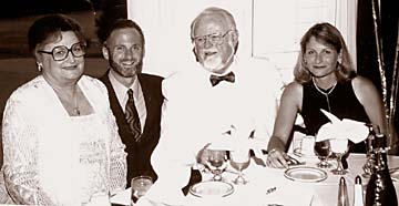 The Dobkins with son and daughter dressed formal, sitting at dinner table with champagne and glasses in foreground