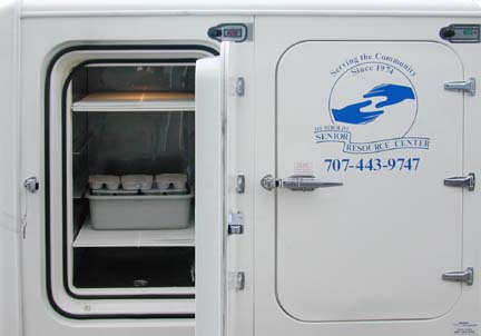[back of delivery van showing open door and packaged food on shelves]