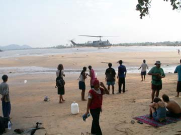[helicopter landing on beach, survivors in foreground on beach]