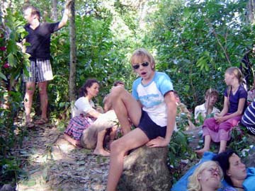 [kids and adult survivors sitting on rocks in shrubs]