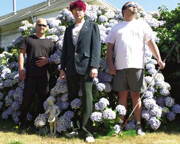 [James Forbes holding cane and standing in front of hydrangea bush with two bandmates]