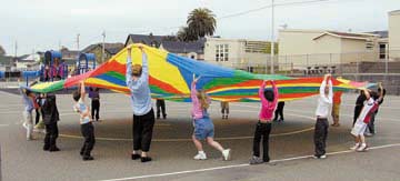 [kids and teacher holding parachute in playground]