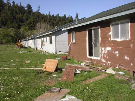 [photo of dilapidated cabins with scrap wood on the ground and painting partially finished]