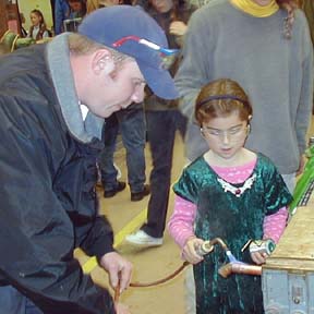 Girl using blow torch with man looking on