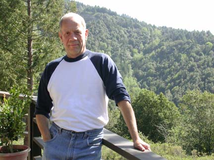 [Peter Dal Poggetto standing on deck of his house, vista of trees and hills in background]