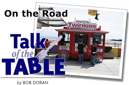 Heading: Talk of the Table, On the Road, by Bob Doran, photo of deep fried Twinkie stand on Santa Cruz Boardwalk