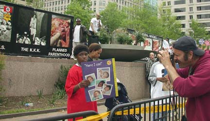 [poster with photos of Nazi and KKK violence and aborted fetus, labeled "Planned Parenthood", and counter-protestors in foreground holding signs with photos of babies]
