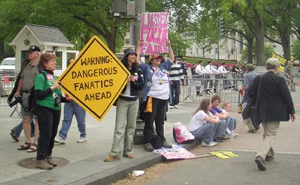 [people on sidewalk holding signs reading "Warning: Dangerous Fanatics ahead"]
