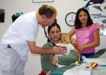 [Doctor with stethoscope listening to baby's heart, while mom and older daughter look on]