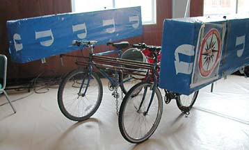 Kinetic sculpture consisting of two connected bicycles and large floats on either side