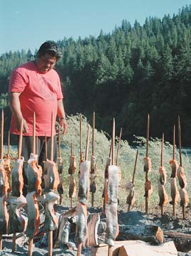 [man cooking salmon on sticks over fire]