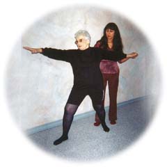 Phyllis Nunes in standing yoga pose, receiving assistance from Elsa Rubio