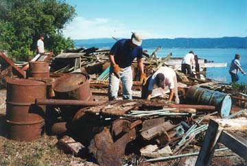 [people moving scrap metal, oil cans and trash from island site]