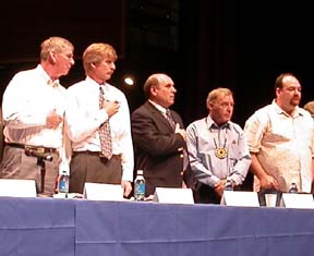 [men on panel, behind long table]