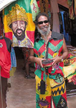[Bongo Ras Star in front of his booth of textile artwork]