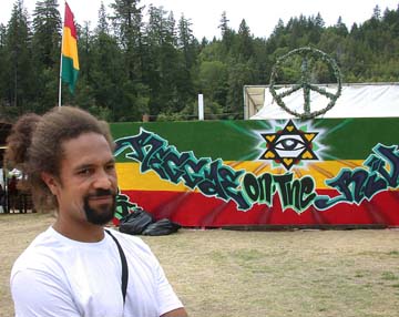 [Diev Hart standing in front of Reggae on the River banner ]