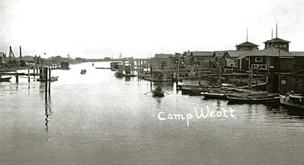 [photo of Camp Weott, buildings, boats and docks at river's edge]