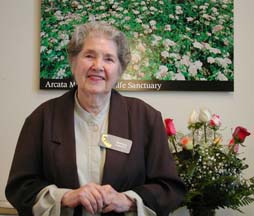 Muriel Hayes standing next to Arcata Marsh poster and rose bouquet