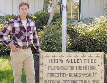 [Mark Higley standing next to Hoopa Valley Tribe sign reading "Hoopa Valley Tribe - planning for the future, forestry - roads - realty, natural resources - building"]