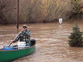 Man in canoe, in flood waters, with top of 35MPH sign above the water in background